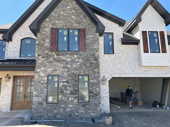 Modern two-story house under construction with stone and siding, open garage, and workers visible inside