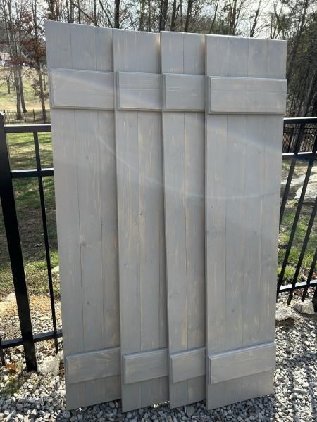 Stacked light gray folding privacy screens outdoors by a black metal fence.