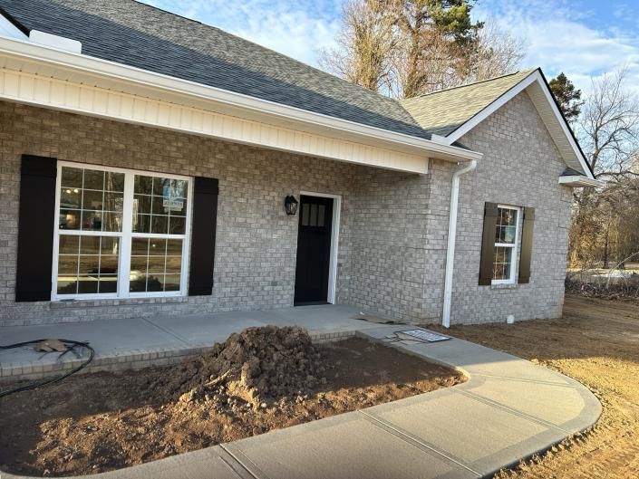 Front porch of a gray brick house with black door, large window, and curved concrete walkway
