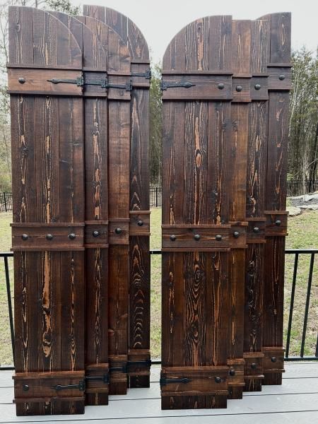 Two dark wooden gates with arched tops, standing open outdoors by a black metal fence.