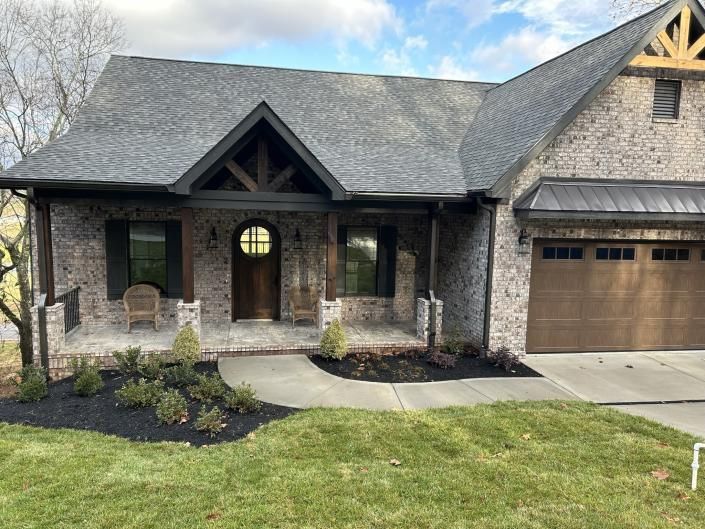 Stone suburban house with front porch, arched doorway, and attached garage under a partly cloudy sky