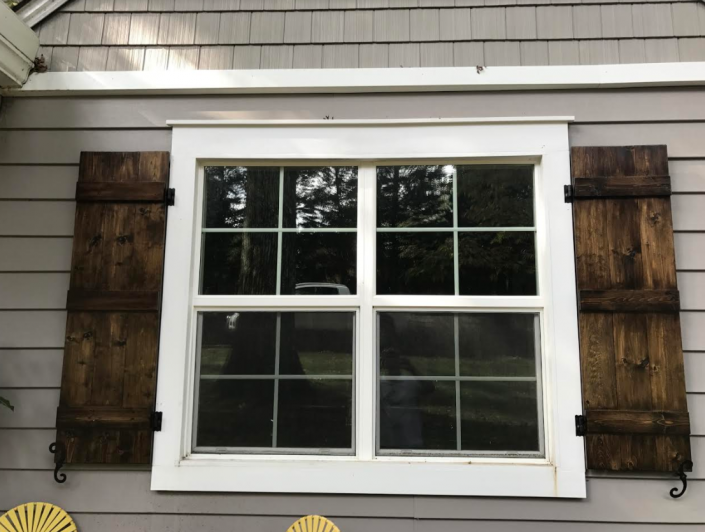 White-framed window with black shutters on a gray shingled house exterior