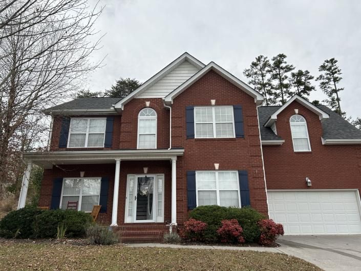 Two-story brick house with white trim, front porch, and a white garage on a cloudy day