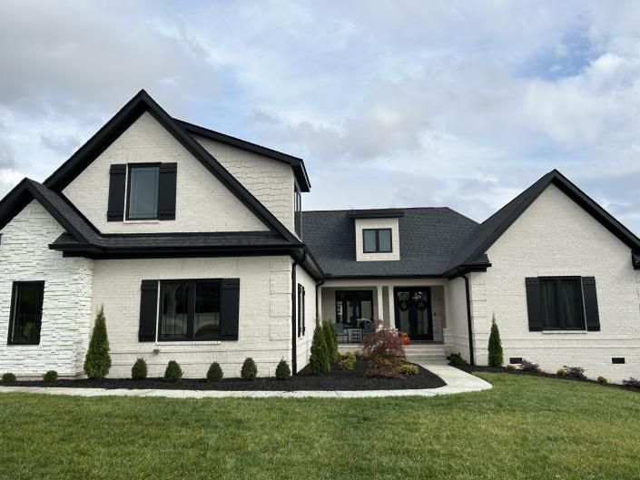 Modern white house with black trim, front lawn, and central entry under a cloudy sky