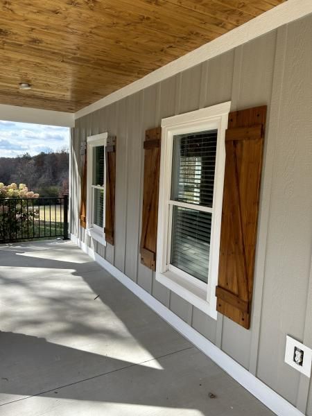 Covered porch with gray siding, wooden ceiling, windows, and a concrete floor overlooking a wooded view