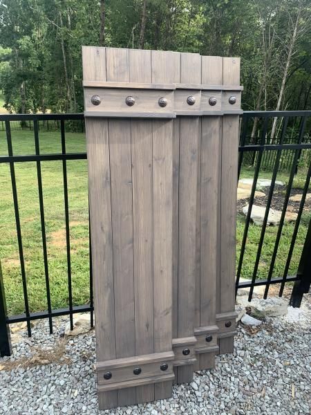 Wooden gate panel with metal studs leaning against a black fence in a gravel yard.