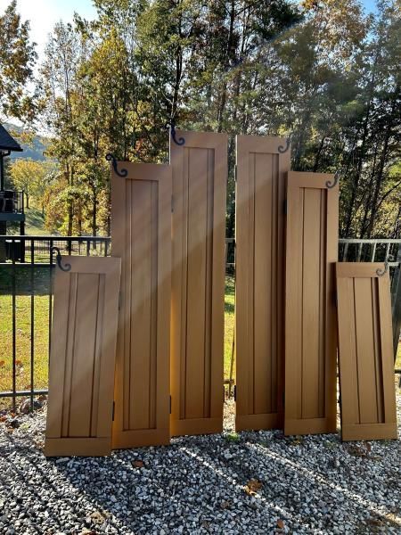 Several brown wood panels leaning outdoors on gravel, with trees and a fence in the background