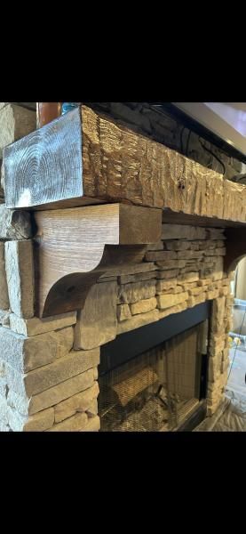 Close-up of a rough-hewn wooden fireplace mantel with a corbel support and stone hearth below