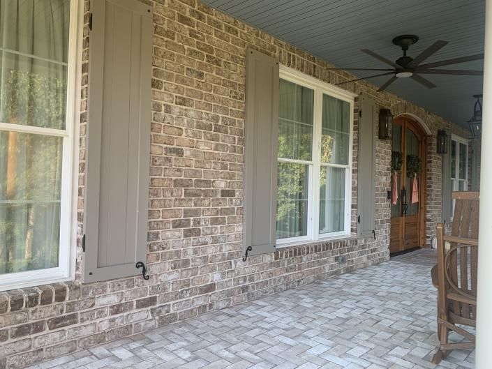 Brick front porch with large windows, shutters, and ceiling fan