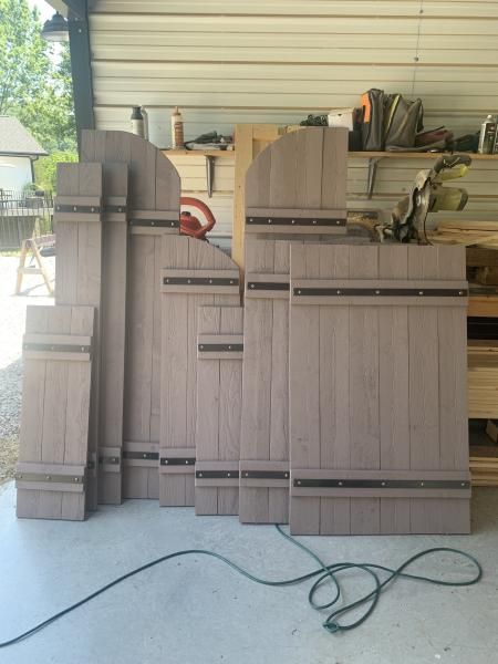 Stacked gray wood panels on a porch with a coiled hose in front.