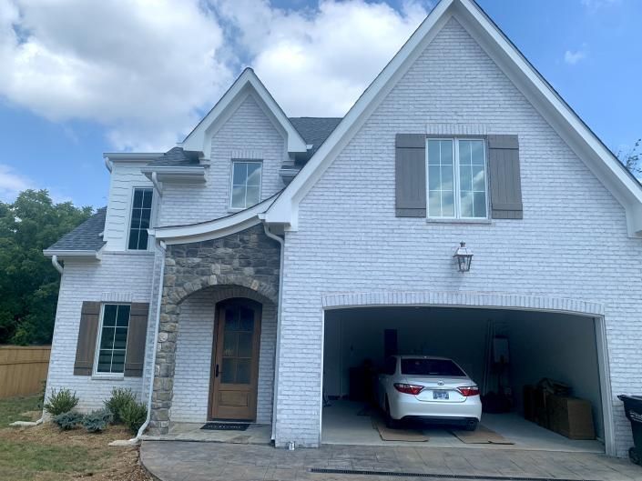 White two-story house with stone entry and an open garage containing a white car