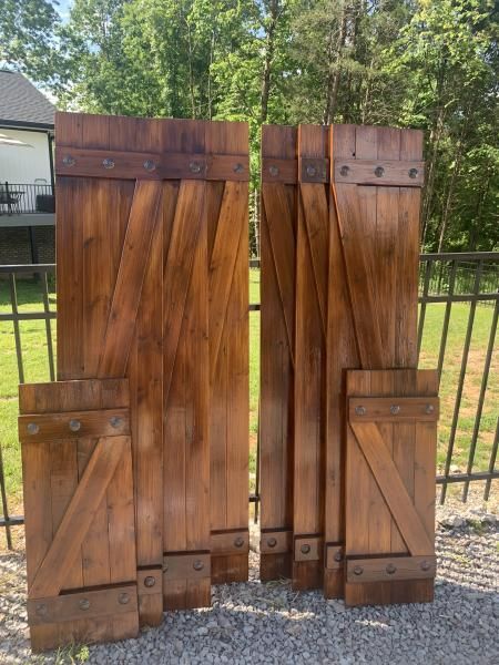 Two wooden doors leaning outdoors on gravel, with a black metal fence and trees behind them.