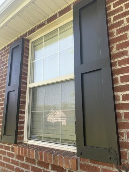 Brick house window with black shutters and white blinds.