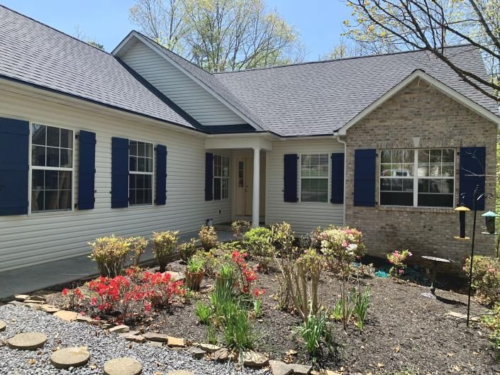 Single-story house with light siding, dark shutters, and a landscaped flower bed in front