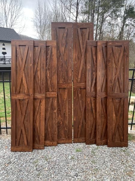 Four wooden decorative panels with chevron carvings, leaning against a black fence outdoors on gravel.