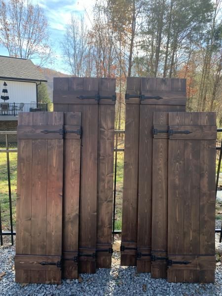 Two dark wooden posts or fence sections standing outdoors in a yard, with trees and a house behind them.