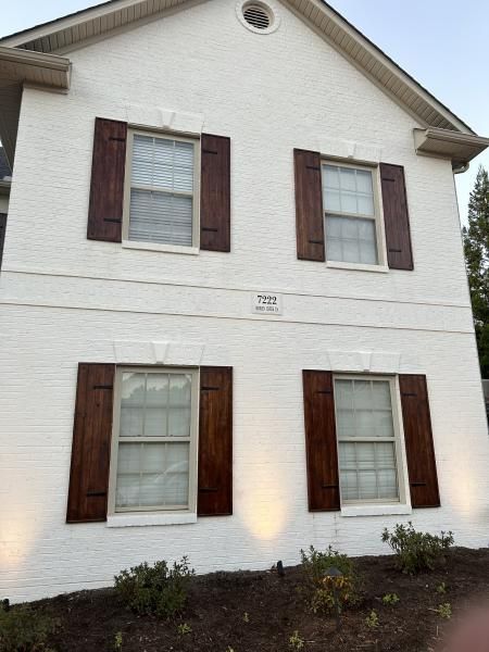Two-story white house with brown shutters and lit exterior lights at dusk