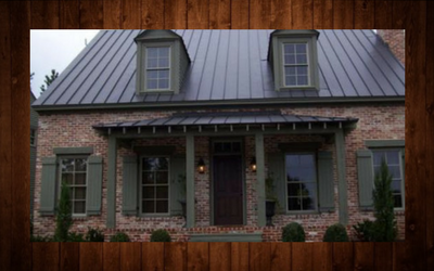 Brick house with a metal roof, dormer windows, and a covered front porch framed by greenery