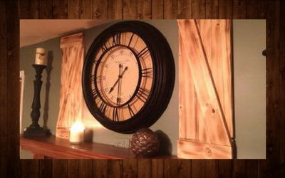Large black wall clock on a mantel with candleholders and warm wooden decor