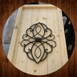 Black wrought-iron decorative wall piece on a light wood panel against a wood background.