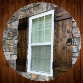 White-trimmed window with shutters set in a rustic stone wall.