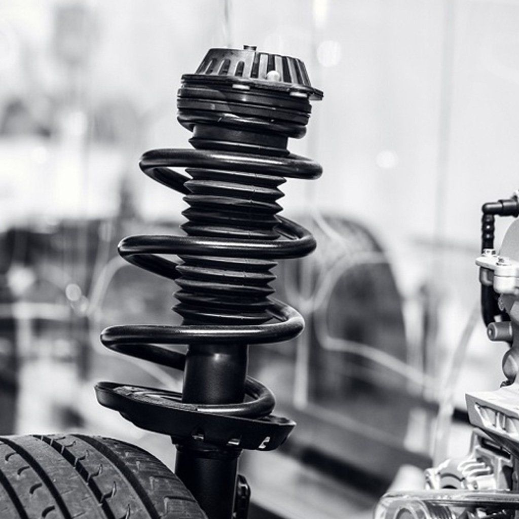 Fotografía en blanco y negro del sistema de amortiguación de un automóvil, que incluye un resorte y un neumático.