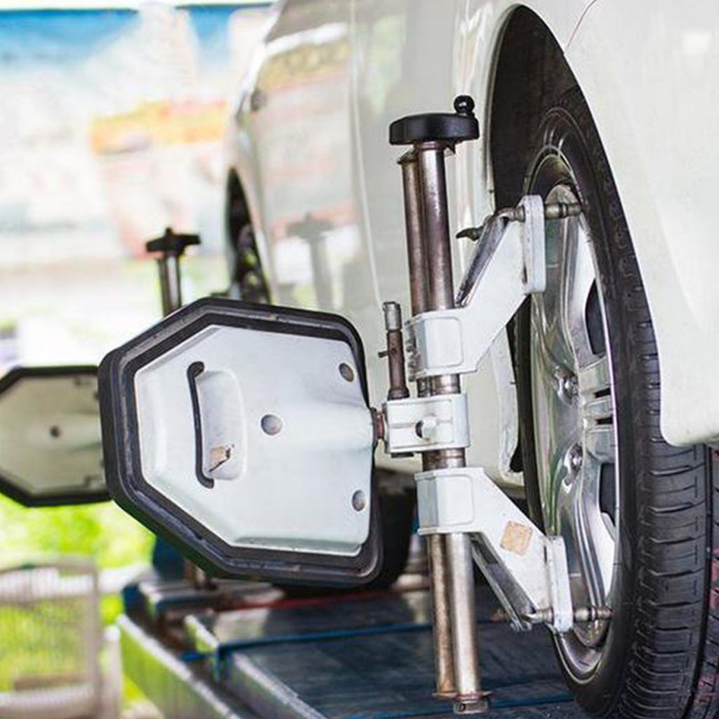 Rueda de coche en revisión de alineación con una máquina acoplada. El coche es blanco y está en un garaje.
