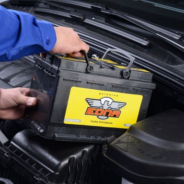 Persona instalando una batería de automóvil nueva con una etiqueta amarilla 