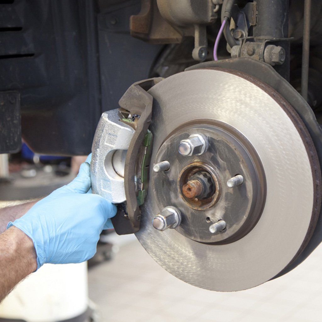 Una persona que lleva un guante azul trabaja en el sistema de frenos de un automóvil, sujetando la pinza cerca del rotor.