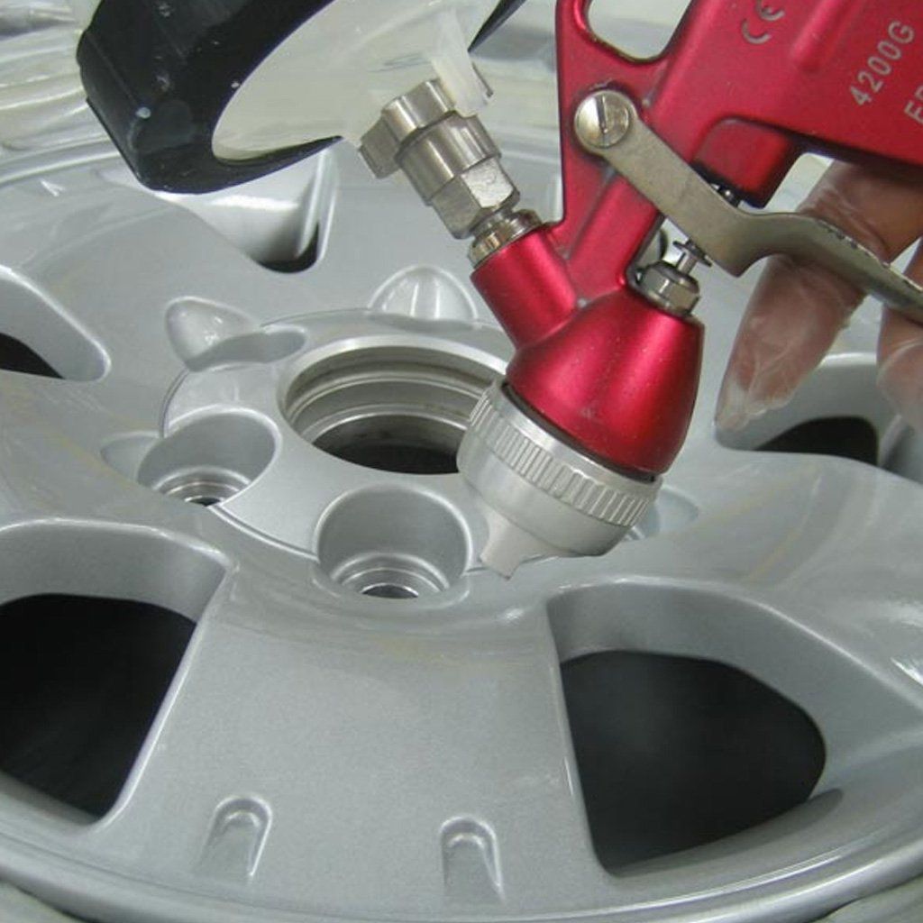Una persona pinta con aerosol una rueda de coche plateada utilizando una pistola pulverizadora roja.