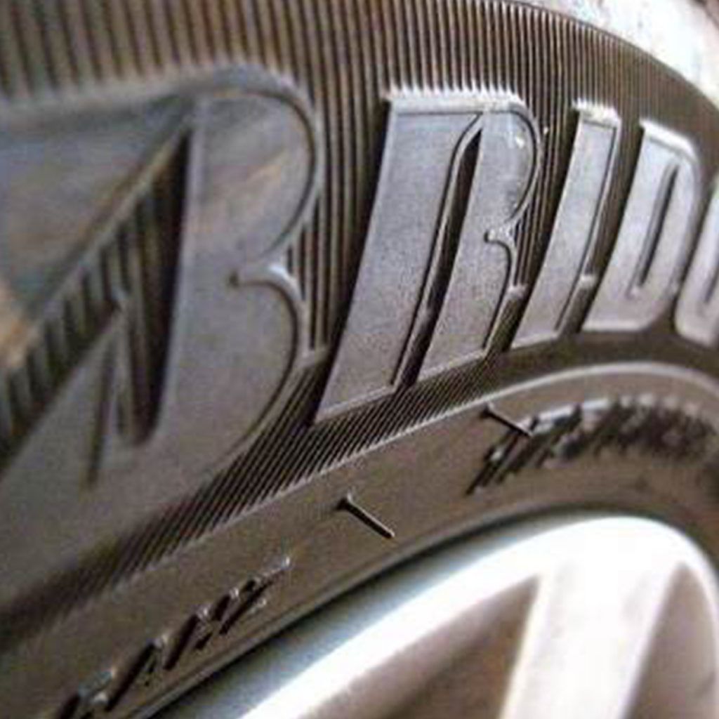 Primer plano de un neumático Bridgestone con el nombre de la marca visible y un clavo incrustado en la banda de rodadura.