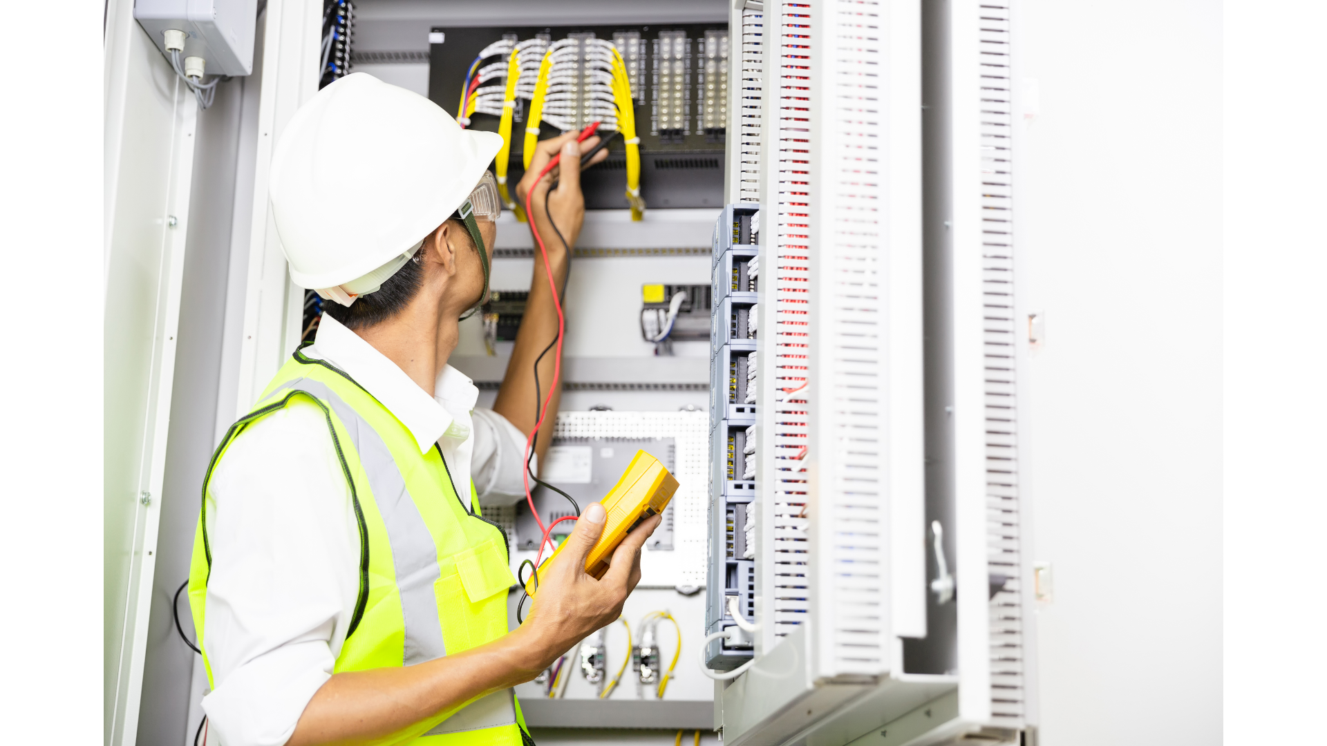 An electrician is working on an electrical box while holding a voltmeter.