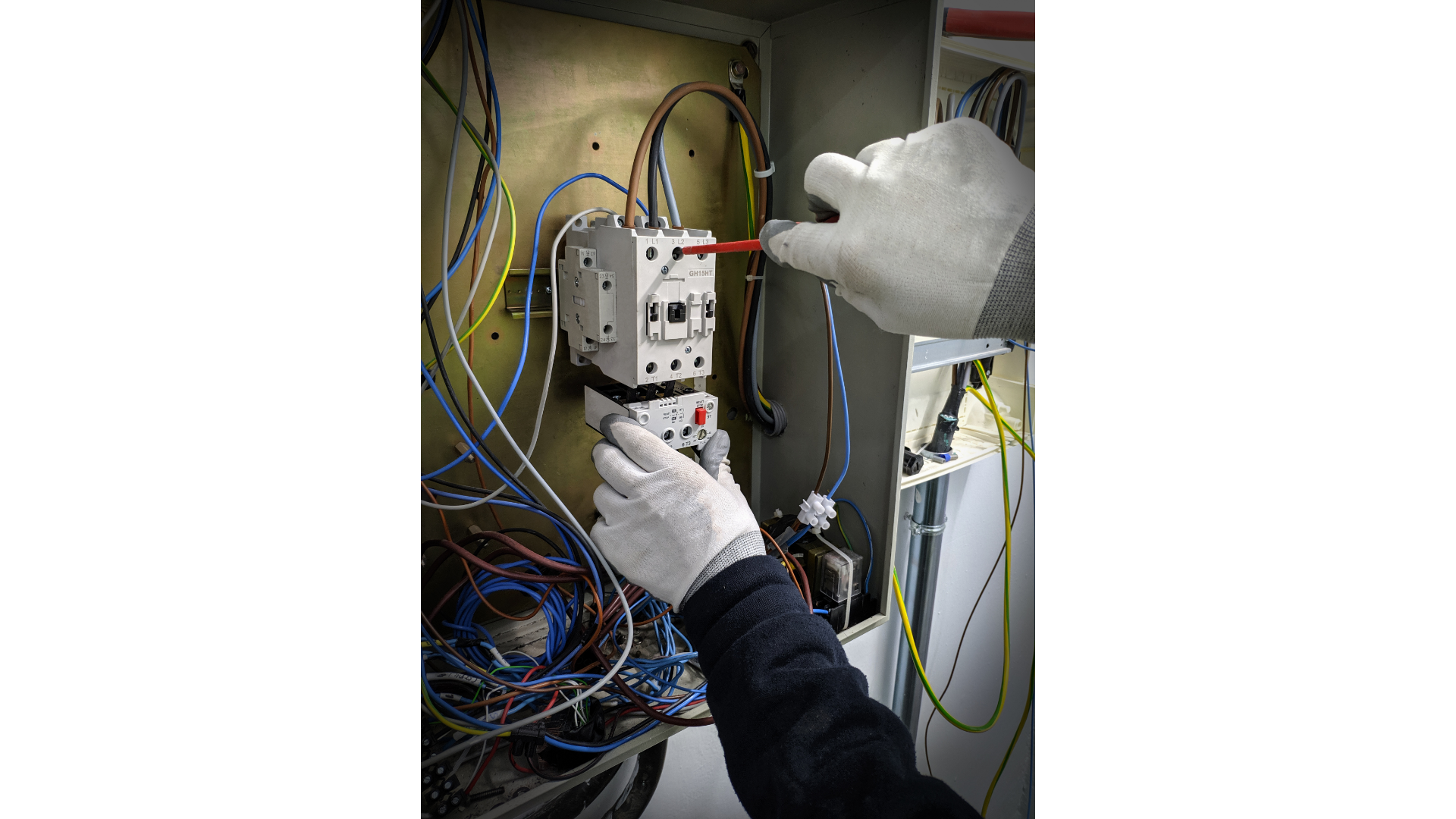 A person is working on an electrical box with a screwdriver.