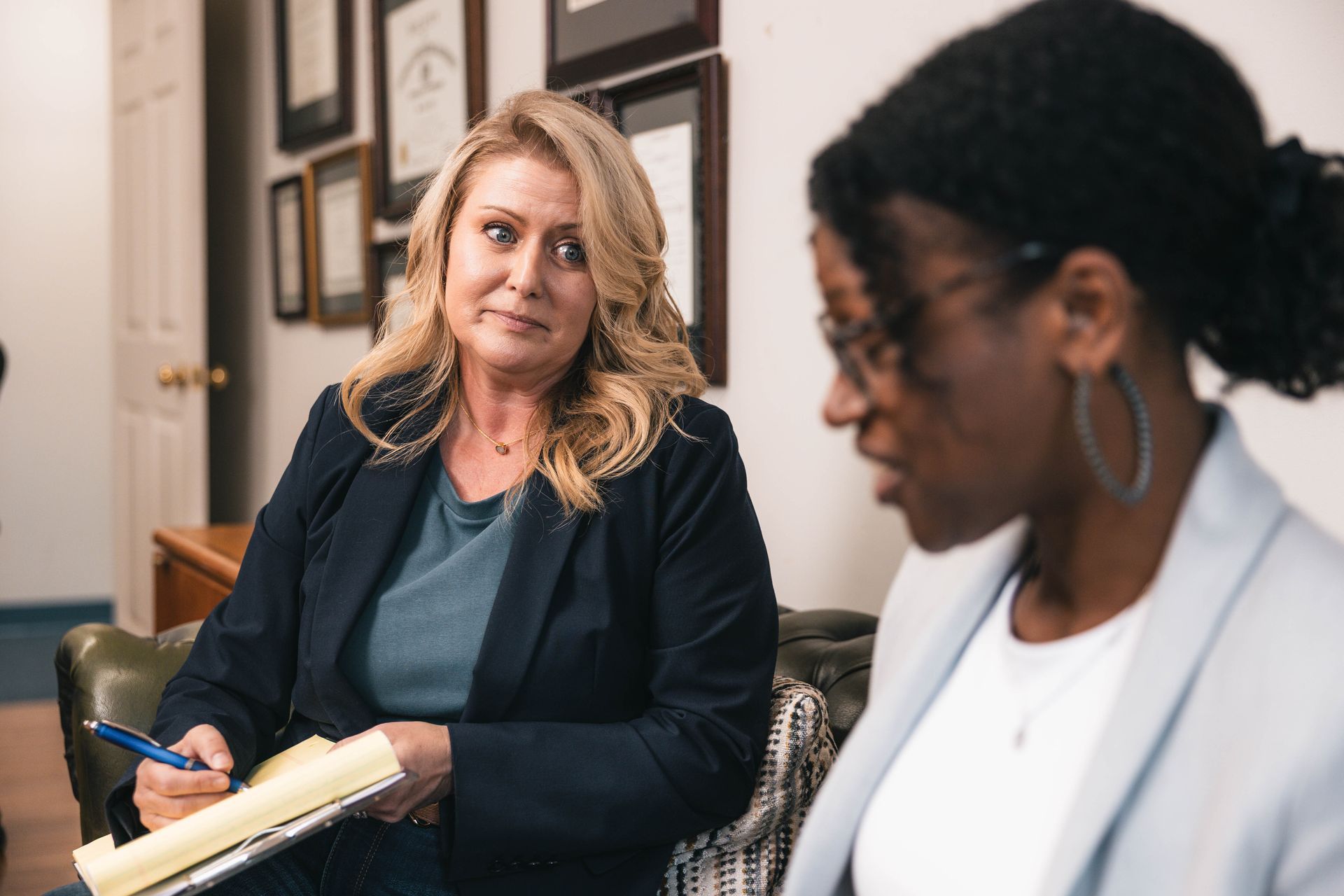 Woman with blonde hair interviewing a Black woman, both in business attire. Office setting.