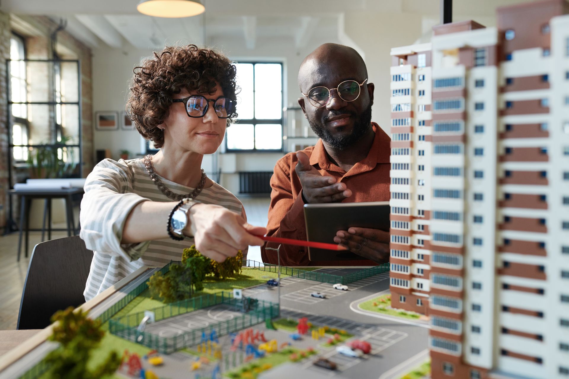 Two architects discussing a building model, pointing at details. Indoors, daytime.