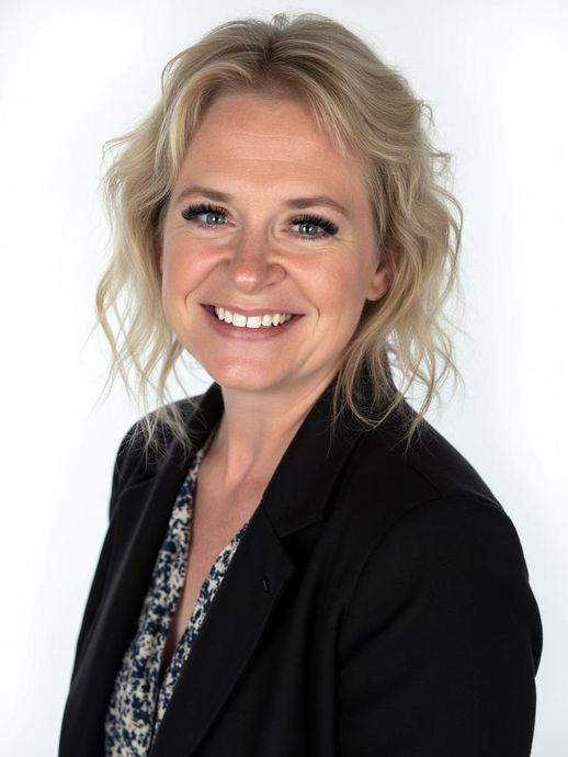 Woman with blond hair, smiling, wearing a black blazer over a patterned top, studio shot.