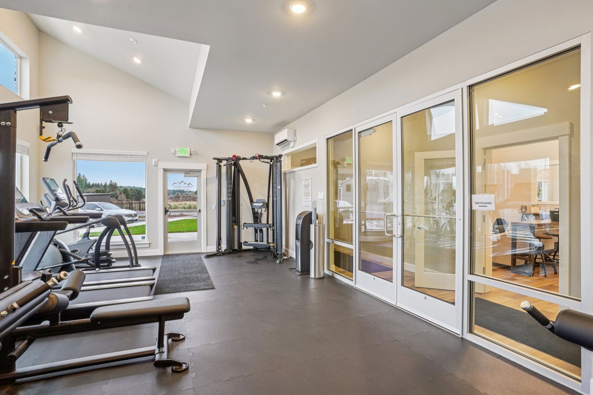Bright gym interior with treadmills, weights, and glass-walled rooms along the right side.