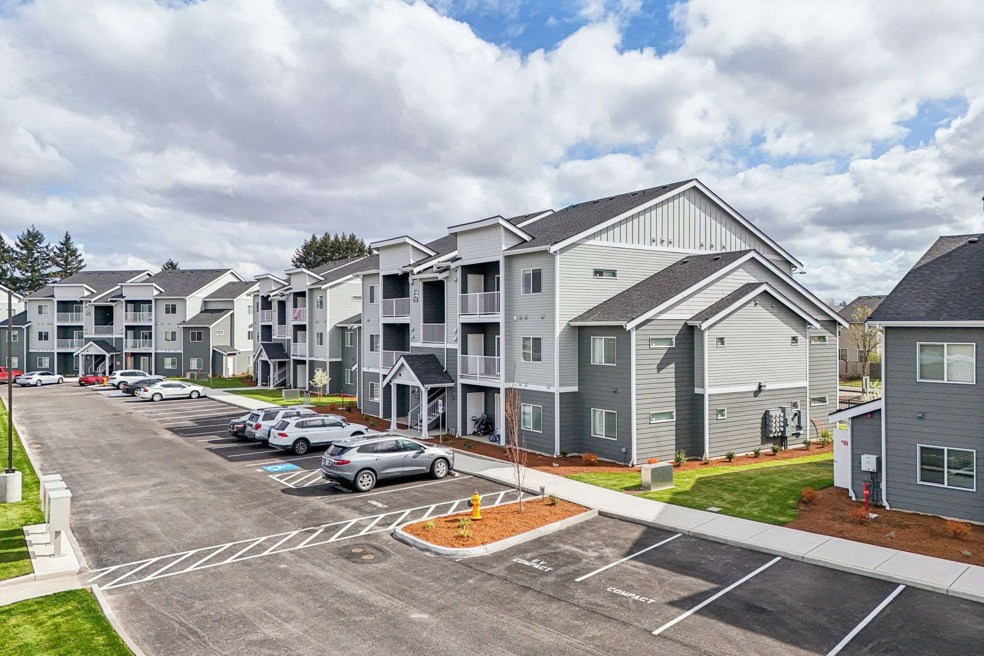 Apartment complex with gray buildings, parked cars, and a cloudy sky