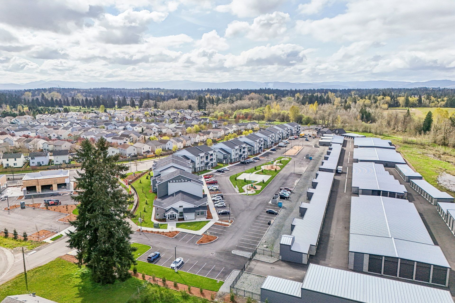 Aerial view of a suburban neighborhood with rows of houses, roads, and trees under a cloudy sky.