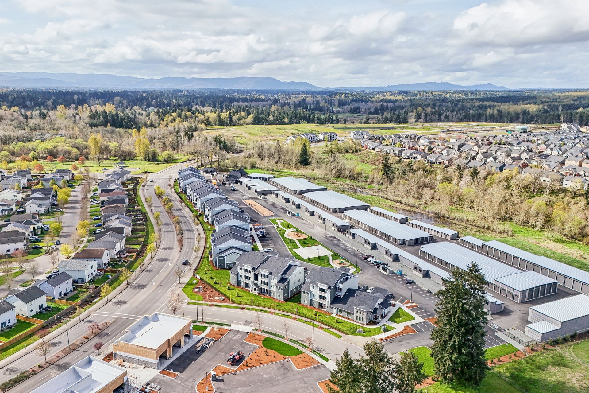 Aerial view of a suburban neighborhood with roads, houses, and green fields under a cloudy sky