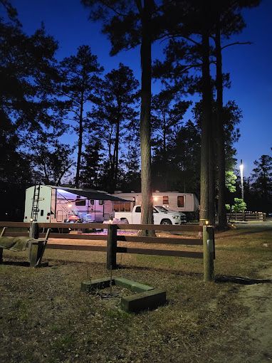 A rv is parked in the woods next to a fence at night.