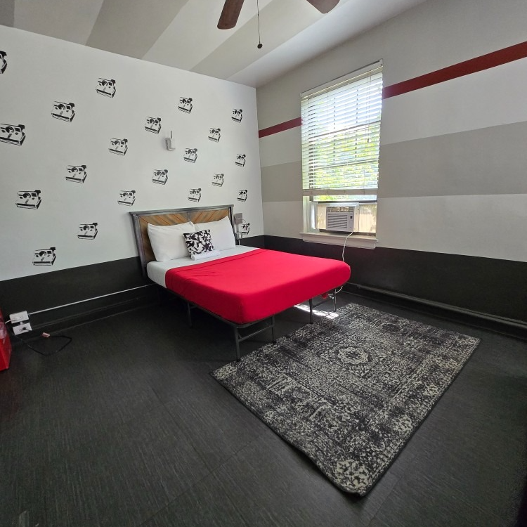 Bedroom with a bed, rug, and decorative wall. Red bedding, dark floor, and black and white wall decals.
