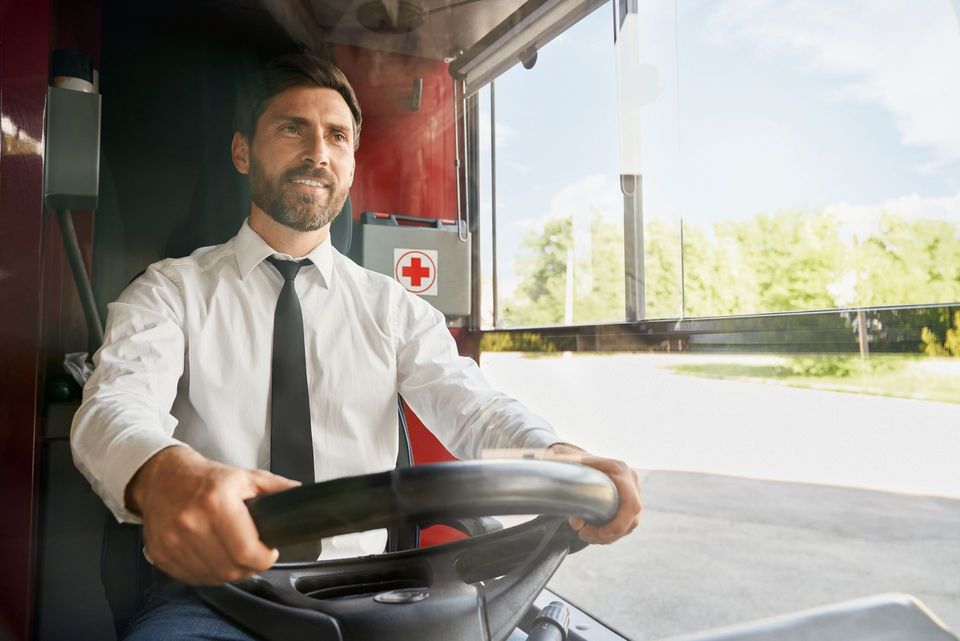 Un conductor de autobús, sonríe mientras sostiene el volante.