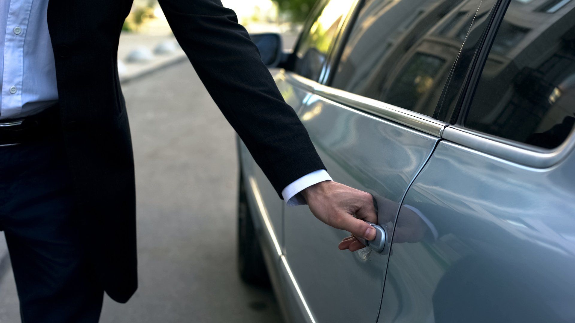 Persona de traje abriendo la puerta de un coche plateado en una calle de la ciudad.