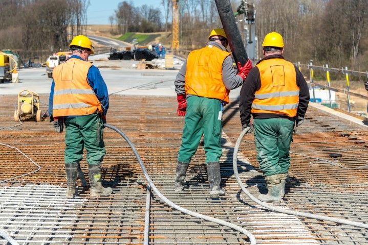 Construction workers pouring concrete on a reinforced steel structure, wearing safety vests and hard hats.