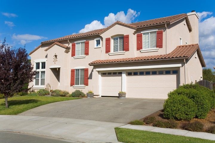 Two-story stucco house with red shutters, tile roof, and a two-car garage on a sunny day.