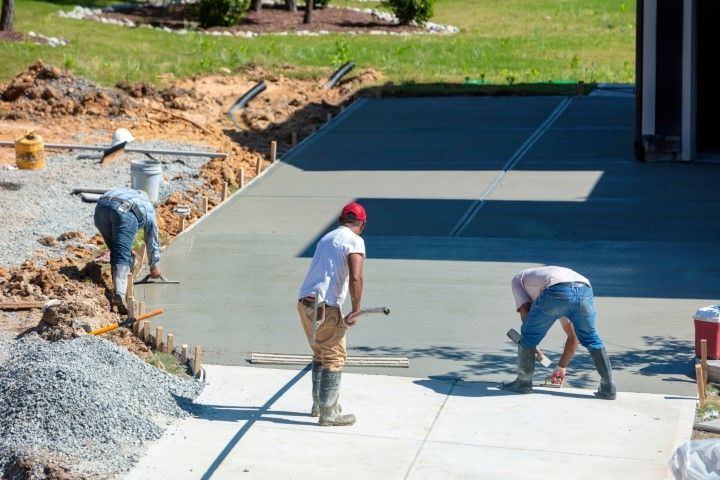 Construction workers smoothing wet concrete driveway in progress.