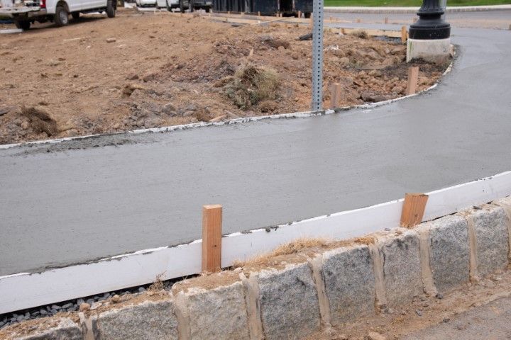 Newly poured concrete sidewalk with retaining wall and dirt background.