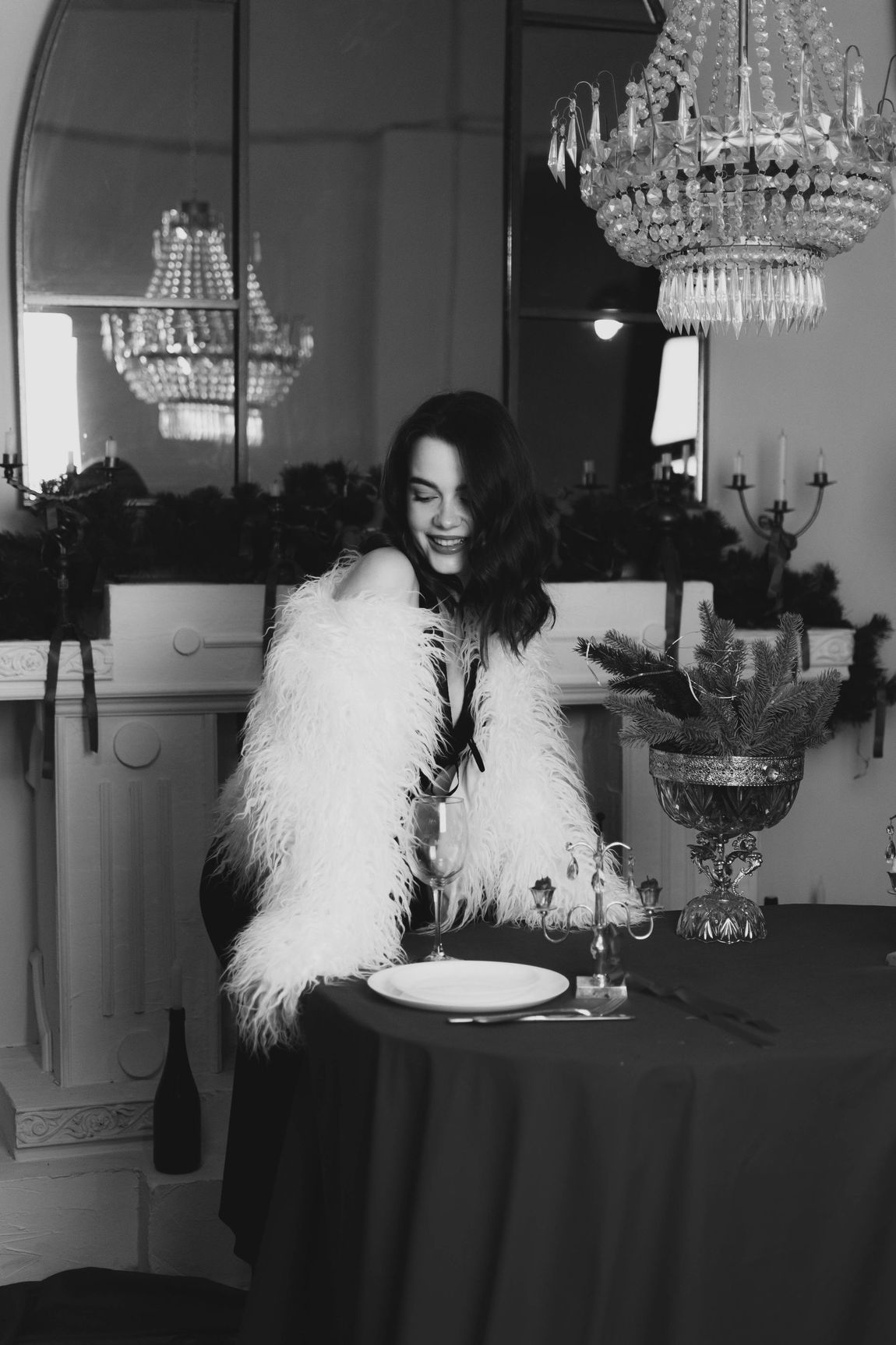 A woman in a fur coat is sitting at a table with plates and glasses.