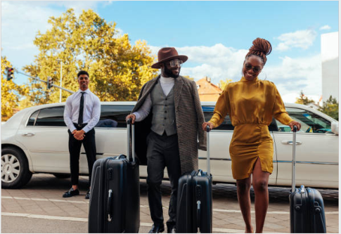 A man and a woman are walking with luggage in front of a limousine.